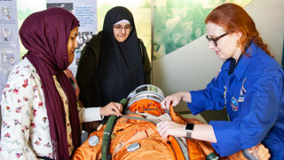 Science Communicator explains how a spacesuit works to two visitors