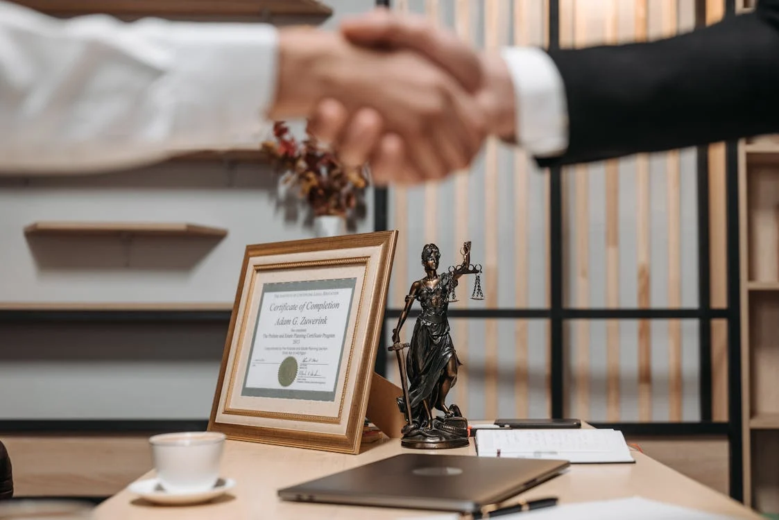 A handshake above a Lady Justice statue on a desk. 