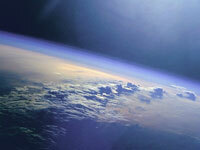 The Earth is observed and some clouds can be seen in it's atmosphere. The Sun's light reflects off the Earth's surface.