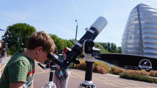 Child looking through a telescope in the car park at the UK in Space festival