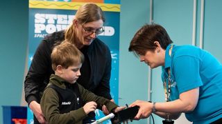 An Education Presenter holding an air pressure control, with a child and their parent interacting with the controller.