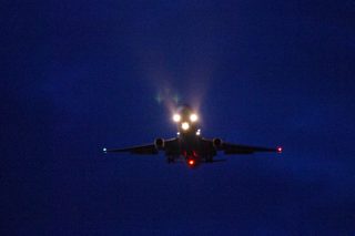 Plane flying at night with three beam lights blazing.