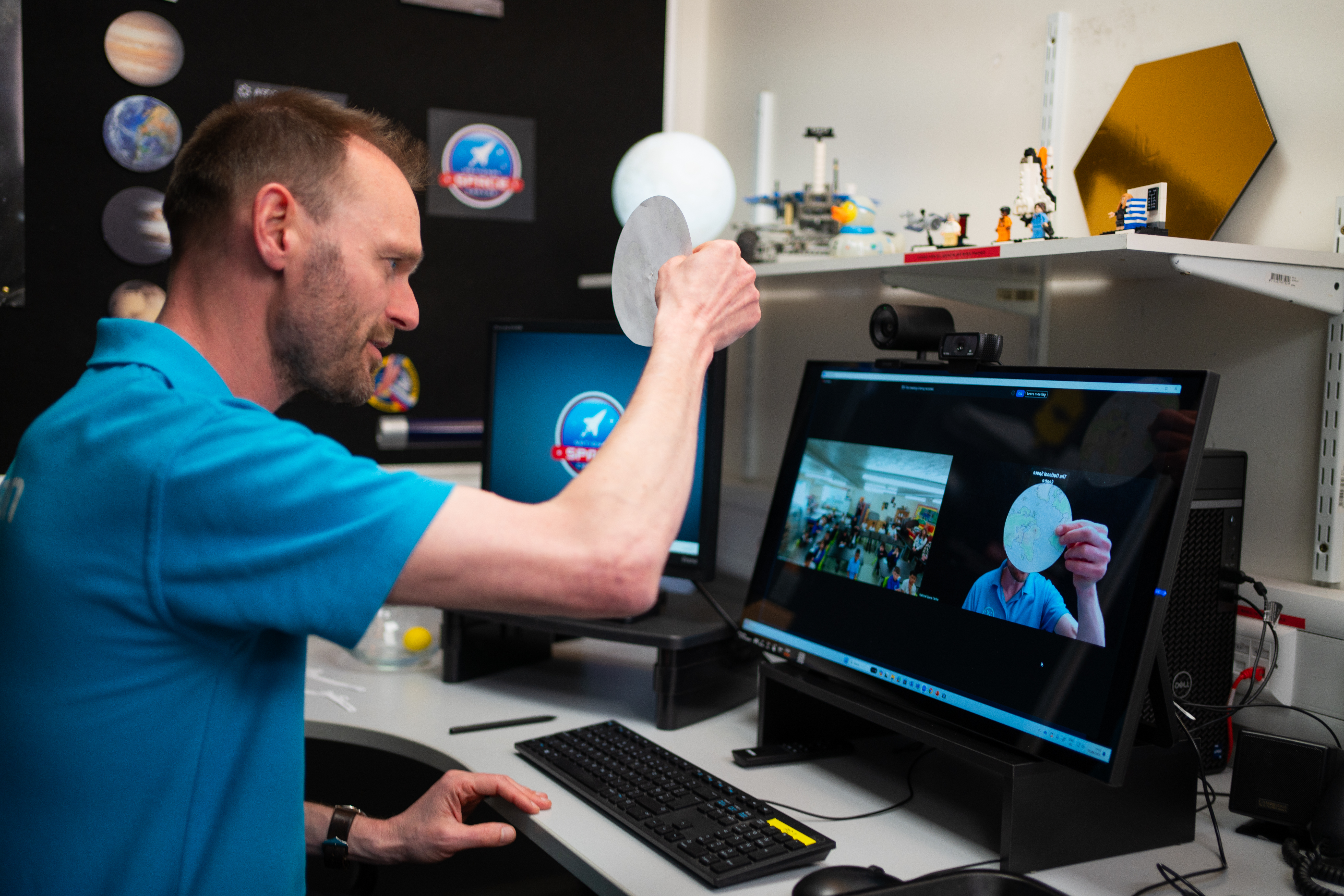 An Education Presenter conducting a Video Conference with a School Group, holding up a circular piece of paper with an image of the Earth on it.