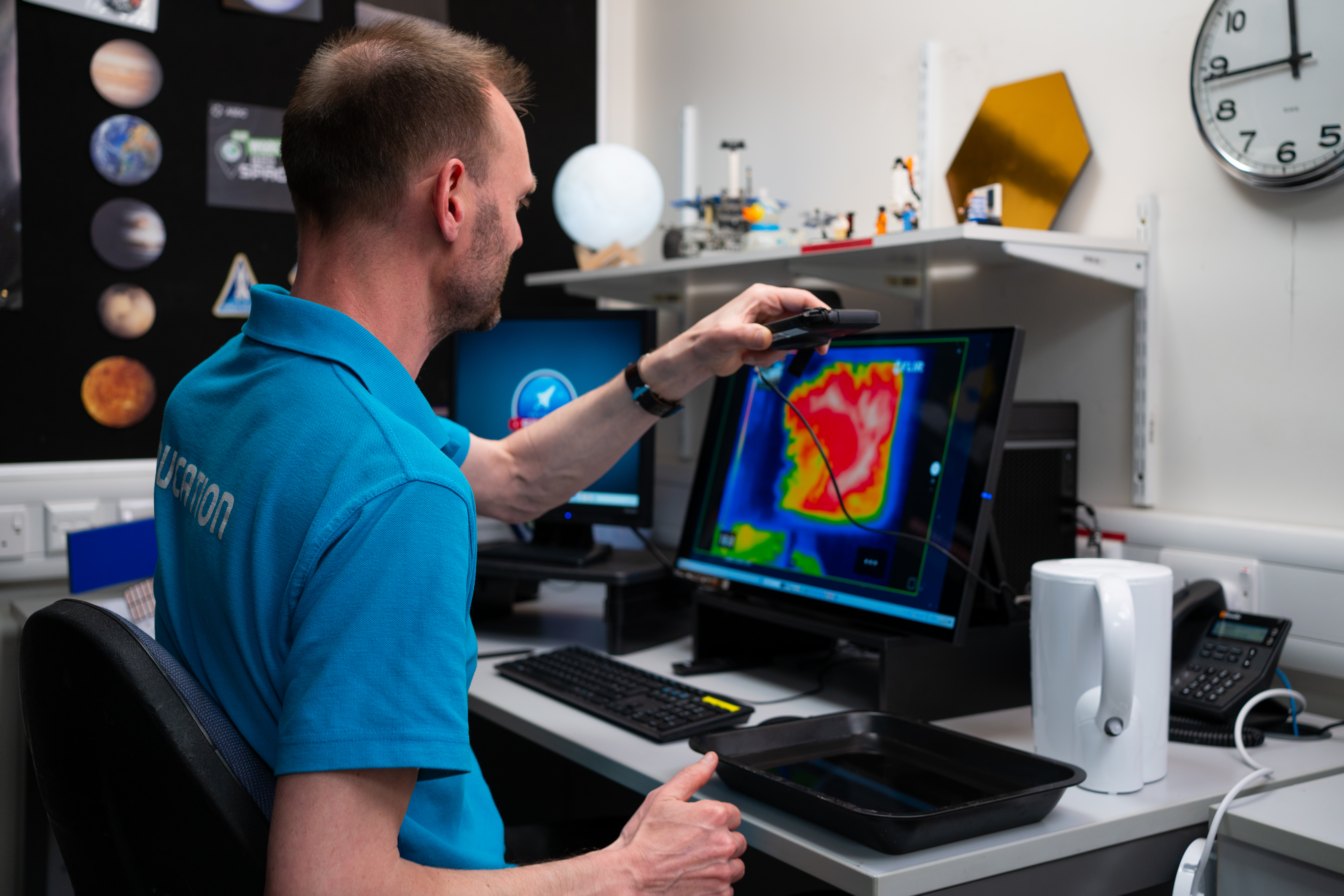 An Education Presenter holding up a thermal imaging camera above some boiled water in a tray, on a Video Conference to a School Group.