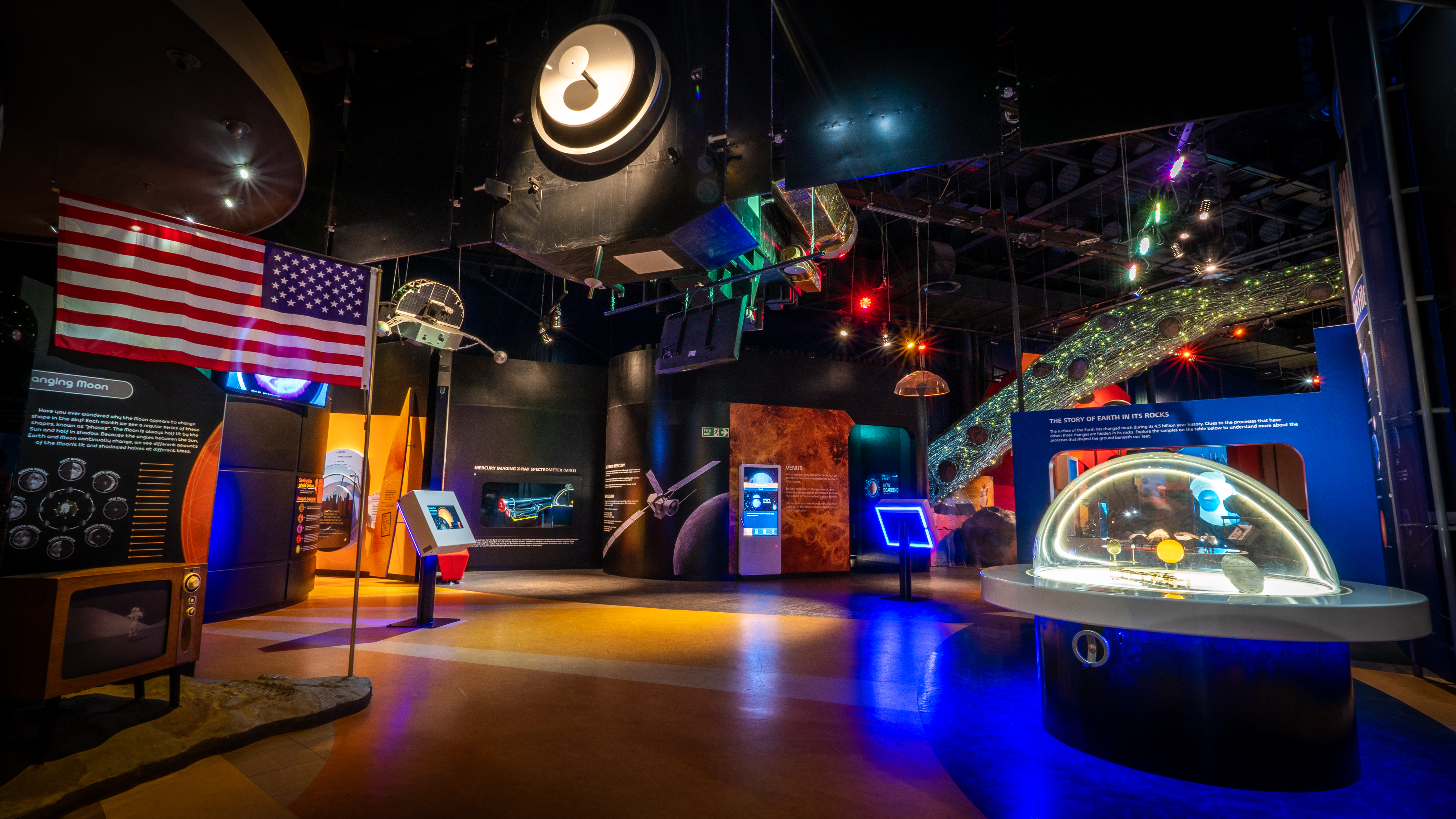 The Our Solar System gallery at the National Space Centre with American flag on a replica Moon surface, orrery, satellites hanging from the ceiling and asteroid belt in the background