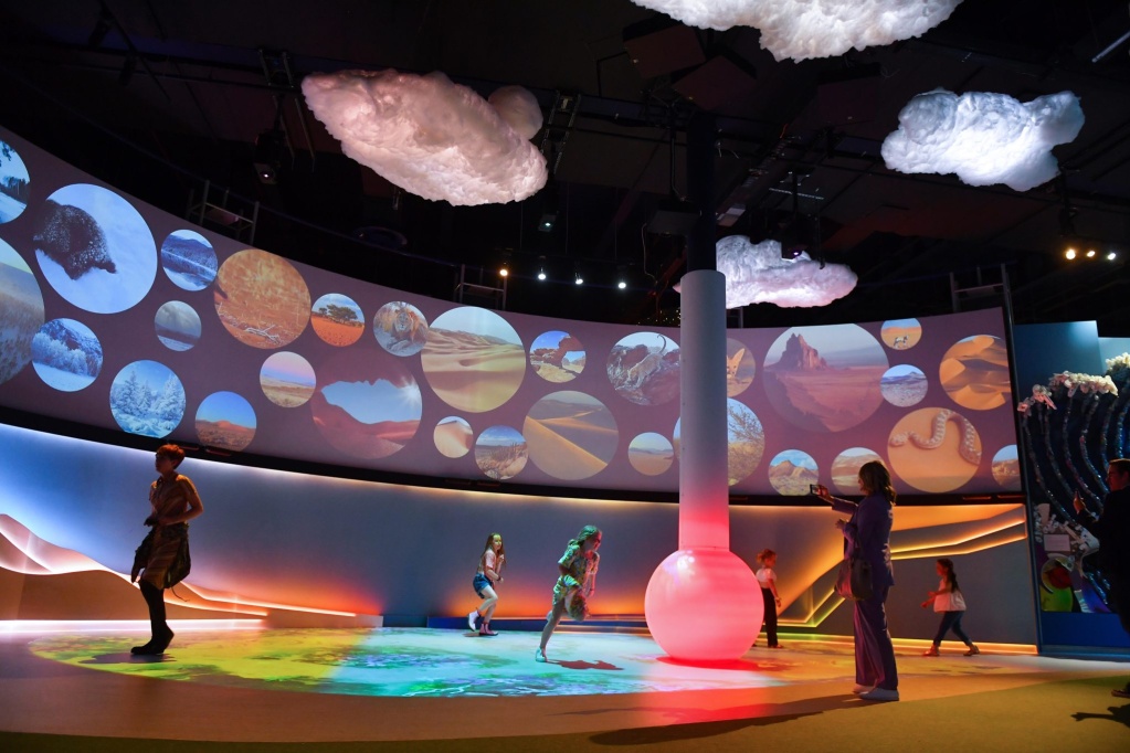 Children playing in the 'Home Planet' gallery at the National Space Centre. A large thermometer model is seen slightly off centre, with synthetic clouds seen above.