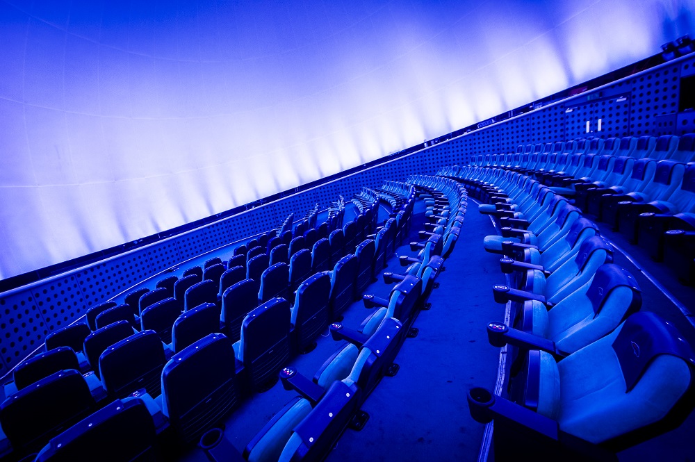 Our Planetarium seats, seen from the side on. The screen is also brightly lit up, with a blue hue.